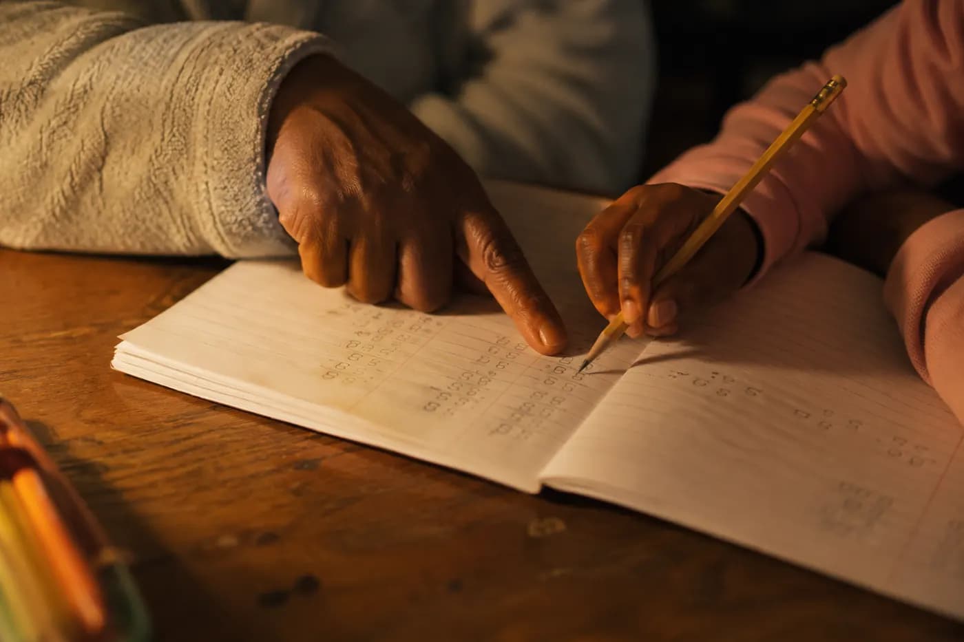 An adult hand pointing at a line in an exercise book beside a child's pencil