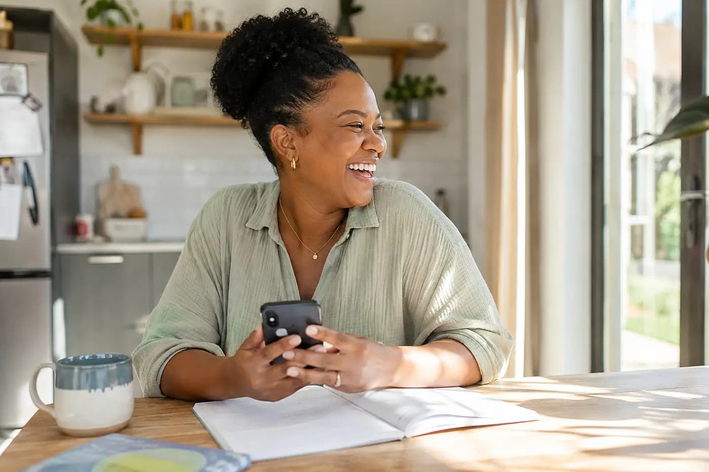 A mother laughing at the kitchen table, phone in hand